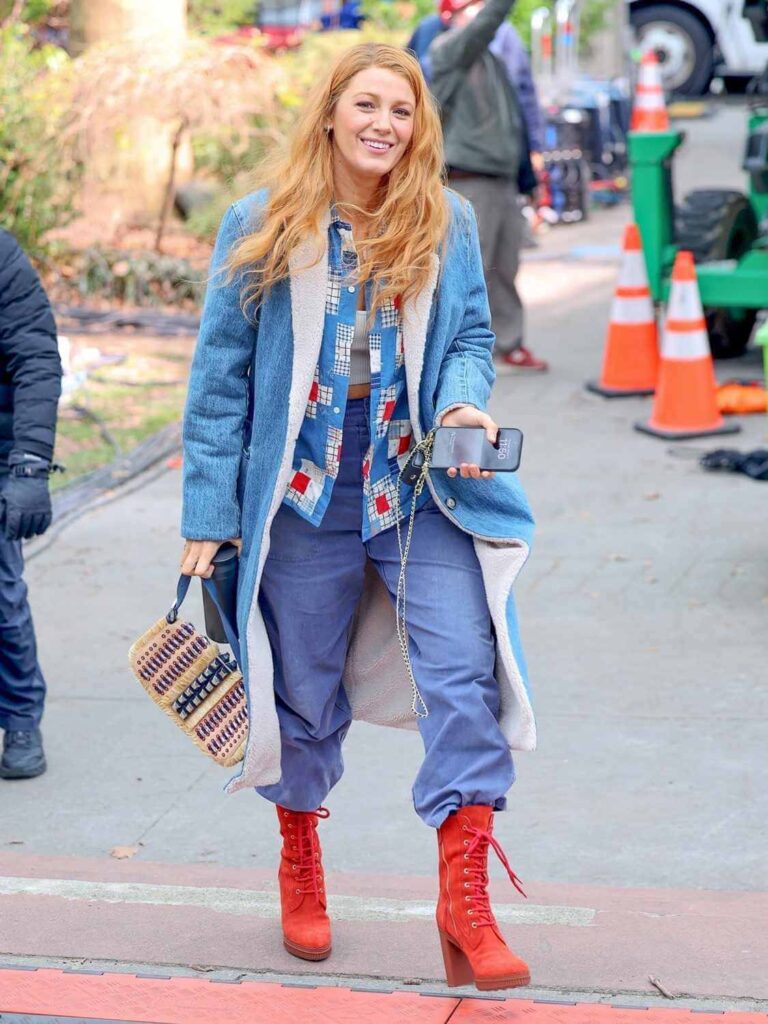 IMG_5148 Blake Lively wearing double denim–a long denim jacket over a patchwork jacket with blue denim pants and tall red platform heeled boots as Lily Bloom in movie adaptation of Colleen Hoover's book "It Ends with Us"